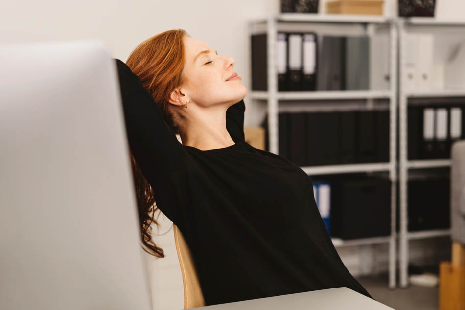 Akademikerin lehnt sich entspannt im Schreibtischstuhl zurück, da sie weiß, dass sie sich mit der Bewerbungsbegleitung keine Sorgen um die Jobsuche machen muss