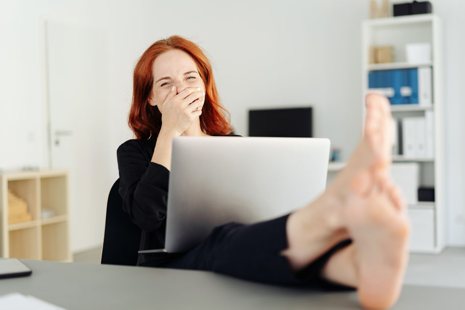 Ein Forscher sitzt lachend vor seinem Laptop mit den Füßen auf dem Schreibtisch und macht ganz entspannt einen Online-Bewerbungskurs.