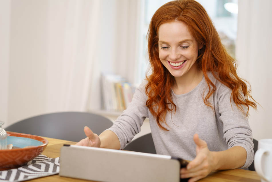 Akademische Jobsucherin nimmt an einer Bewerbungsberatung teil und schaut lächelnd auf den Bewerbungstrainer im Tablet.