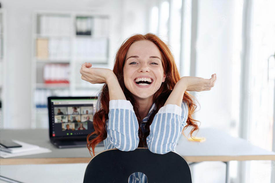 Eine lachende Forschende sitzt vor ihrem Laptop auf dem ein Live-Online-Meeting des Karriereprogramms für Wissenschaftler zu sehen ist