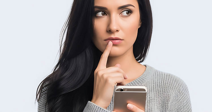 Bewerberin schaut nachdenklich auf das Handy und überlegt, ob sie das Unternehmen anrufen soll, dem sie eine Bewerbung geschickt hat